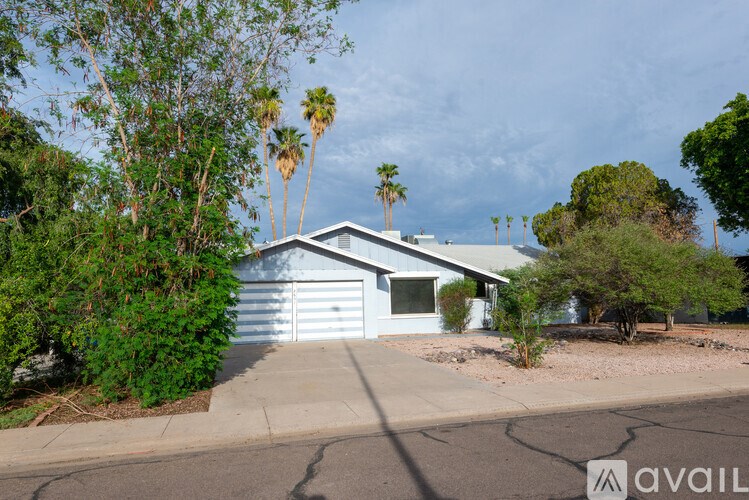 A house with a blue exterior is surrounded by greenery and palm trees.
