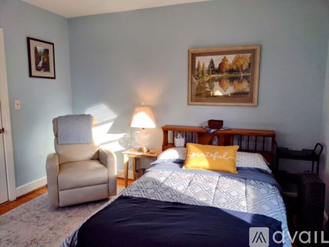 A bedroom with a bed, chair, and painting on the wall.