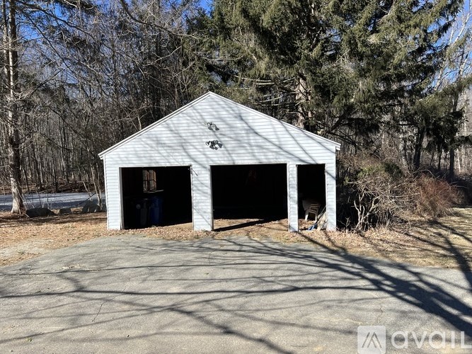 A white garage with a metal roof is situated in a wooded area.
