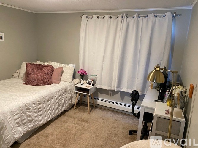 A bedroom with a bed, nightstand, and window with white curtains.
