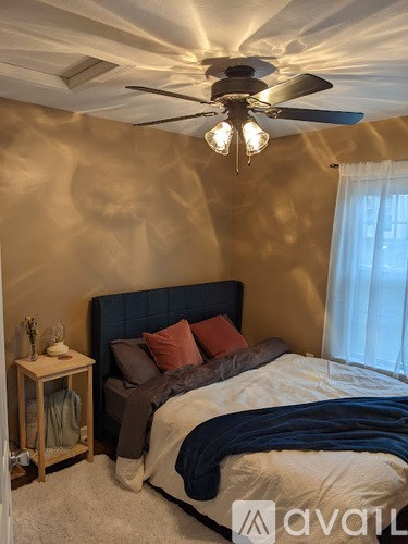 A bedroom with a bed, pillows, a ceiling fan, and a nightstand.