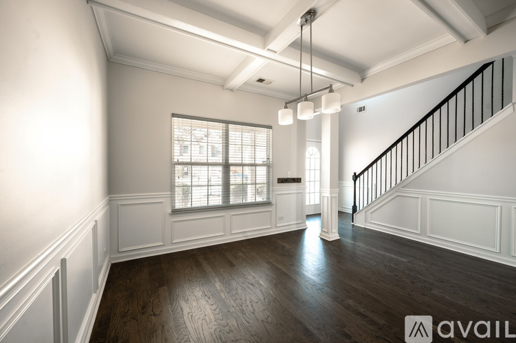 A spacious room with wooden floors and a staircase with black railings.