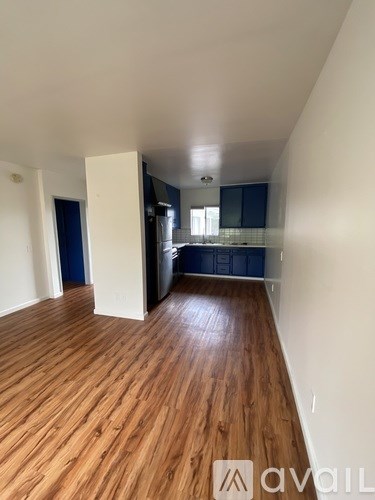 A room with wooden flooring and a kitchen area in the background.