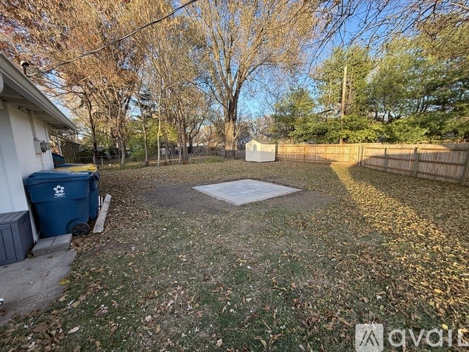 A backyard with a blue trash can and a wooden fence.