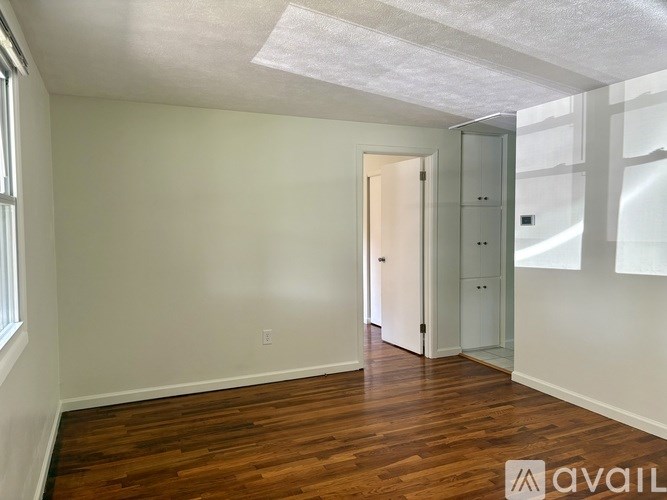 A room with wooden floors and white walls, with a door and a window.