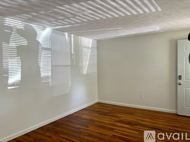 A room with wooden flooring and white walls, with a door on the right side.