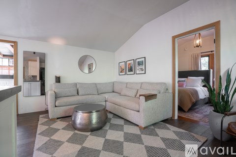 A living room with a grey couch and a round mirror on the wall.