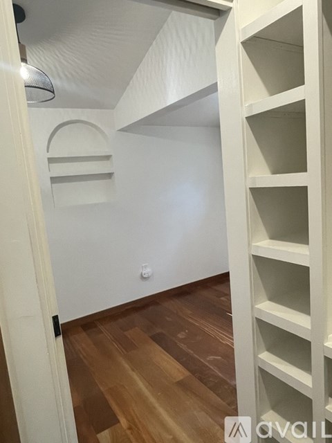 A white shelving unit with multiple shelves is in a room with wooden flooring.