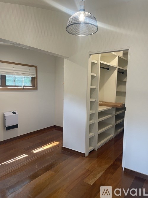 A room with a white ceiling and wooden floor with a white cabinet and a window.