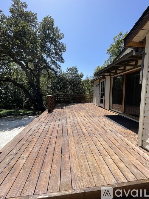 A wooden deck with a house and trees in the background.
