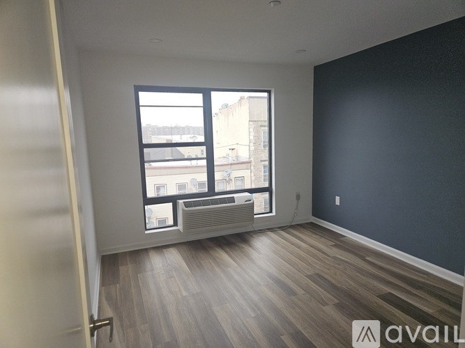 A room with a large window and wooden flooring is available for rent.