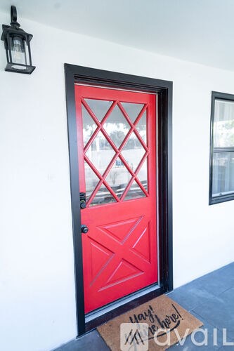 A red door with a black frame and a mat on the floor that says "Welcome".