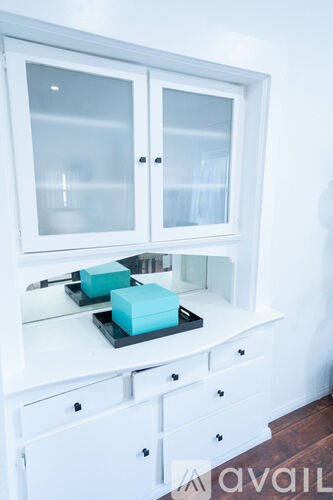A white cabinet with a glass door and a black tray with a blue box on it.