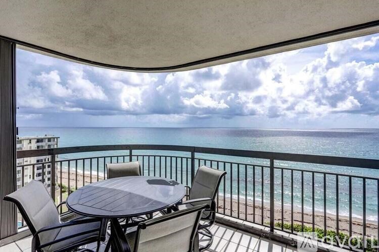 A balcony with a table and chairs overlooking the ocean.