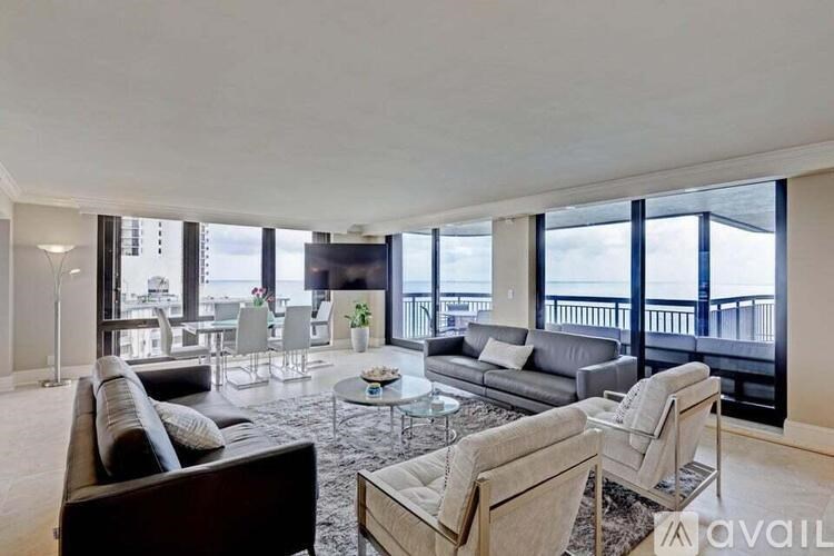 A living room with a large couch, a coffee table, and a balcony with a view of the city.
