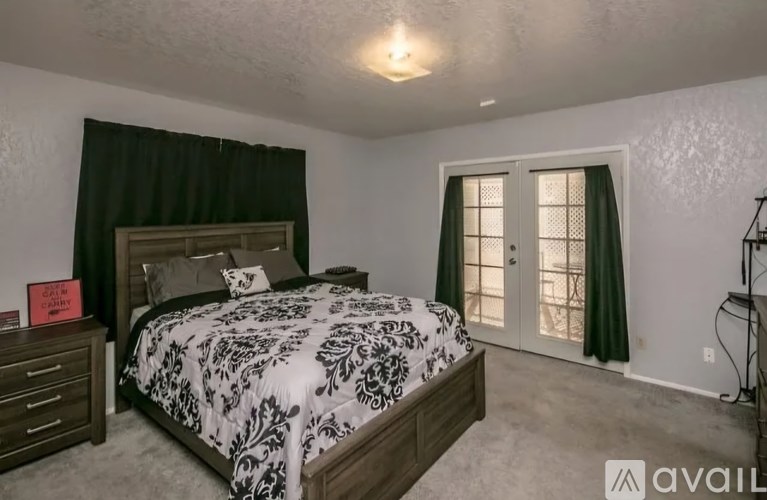 A bedroom with a large bed and a window with green curtains.