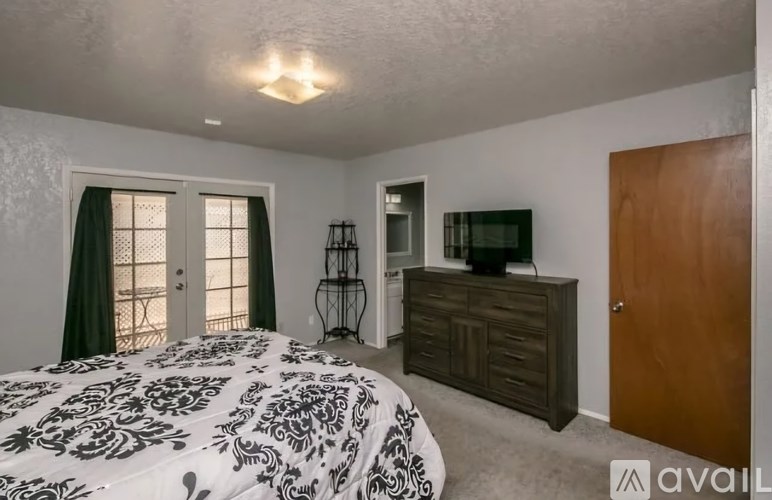 A bedroom with a patterned bedspread, a wooden dresser, and a window with green curtains.