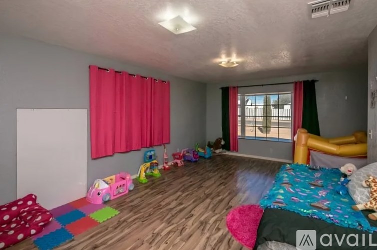 A room with a bed, a window with red curtains, and a wooden floor.
