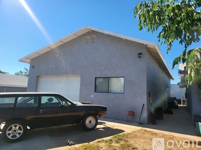 A black car is parked in front of a grey house.