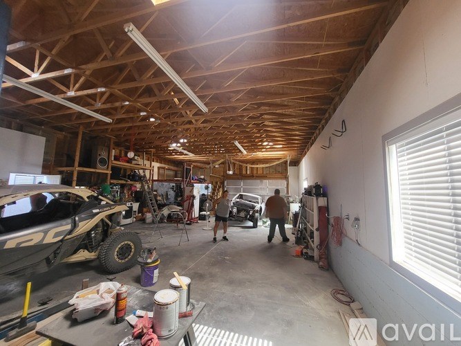 A man is standing in a garage with a truck and a car in the background.