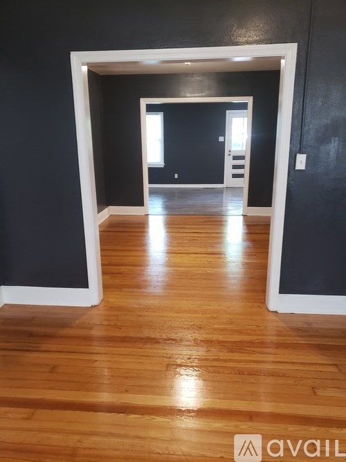 A room with wooden floors and a white doorway leading to another room.