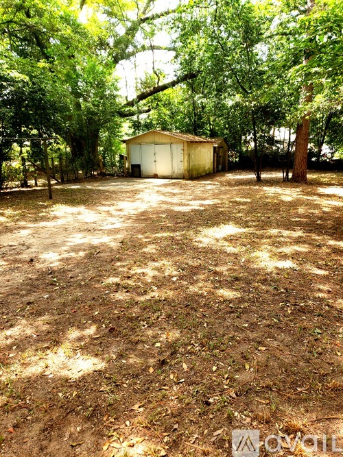 A shed sits in a yard with trees and a fence.