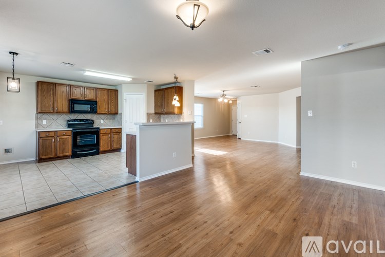 A spacious living room with wooden floors and a kitchen area in the background.