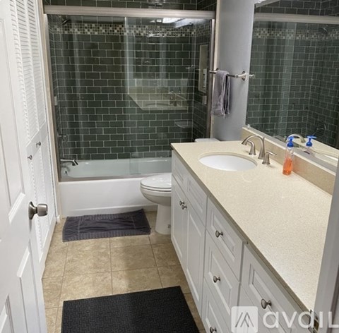 A bathroom with a white toilet, sink, and a black mat on the floor.