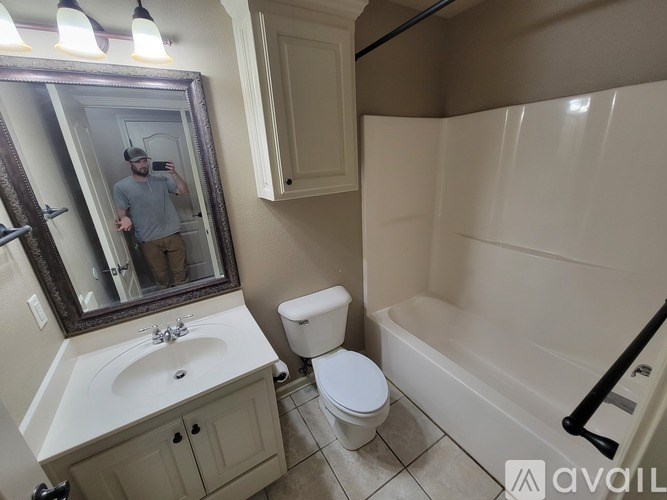 A man is taking a selfie in a bathroom with a sink, toilet, and bathtub.