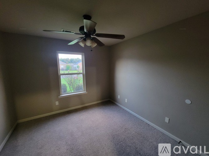 A room with a ceiling fan and a window showing a view of a tree and a house.