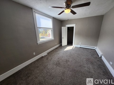 A room with a ceiling fan and a window overlooking a street.