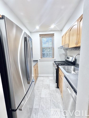 A kitchen with a stainless steel refrigerator and a window with blinds.