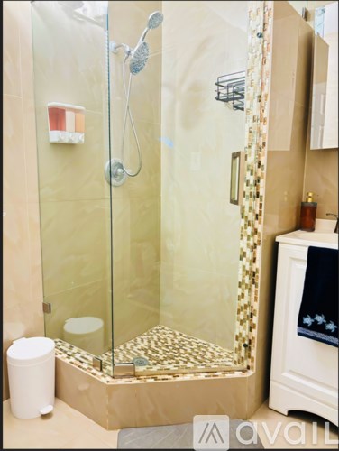 A shower with a glass door and a white bucket on the floor.