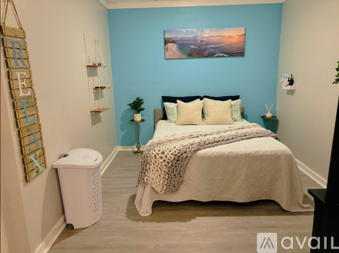 A bedroom with a bed, a nightstand, a trash can, and a wall hanging.