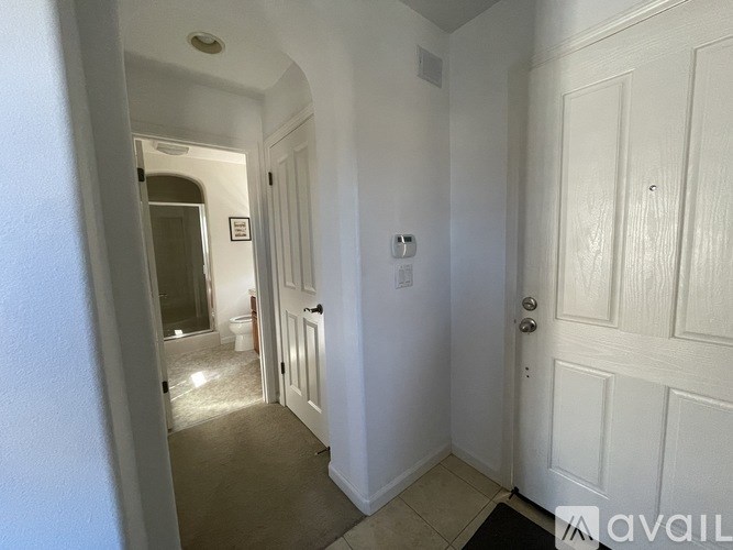 A hallway with a door on the right and a bathroom visible in the background.