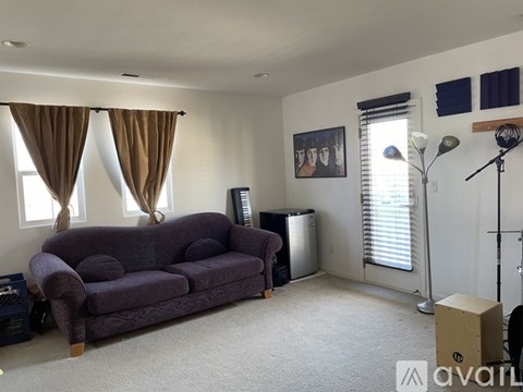 A living room with a purple couch and a painting on the wall.