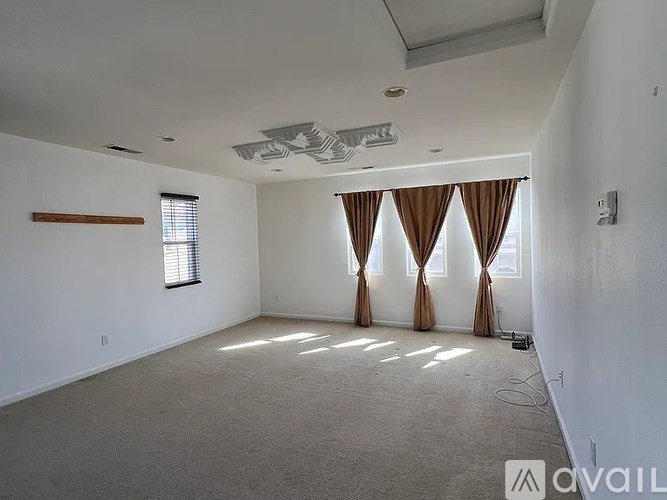 A room with a carpeted floor, a window with brown curtains, and a ceiling fan.