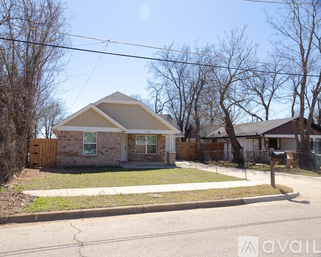 A house with a brown roof and a white door is surrounded by a fence and trees.