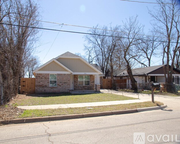 A house with a brown roof and a white door is surrounded by a fence and trees.