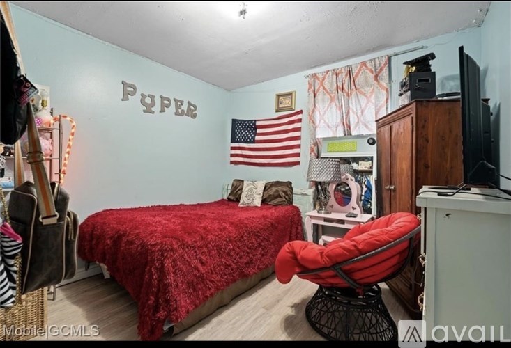 A bedroom with a red bedspread and a red chair.