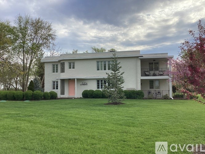 A white house with a red door and a tree in front of it.