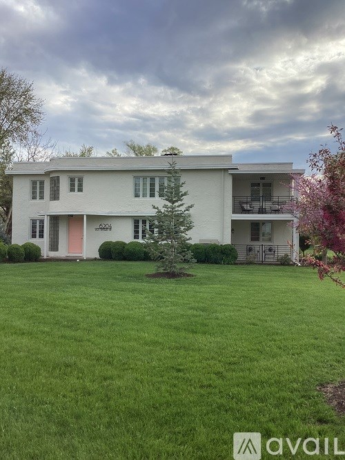 A white two-story house with a red door and a balcony on the second floor.