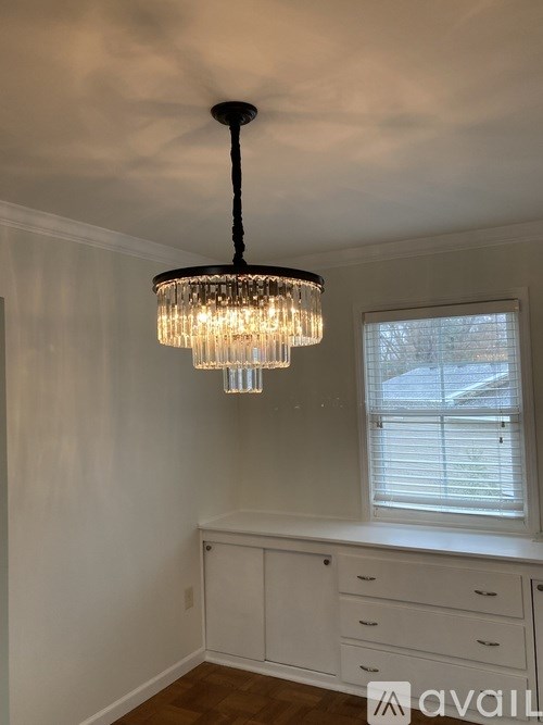 A chandelier hangs from the ceiling in a room with white walls and a window.