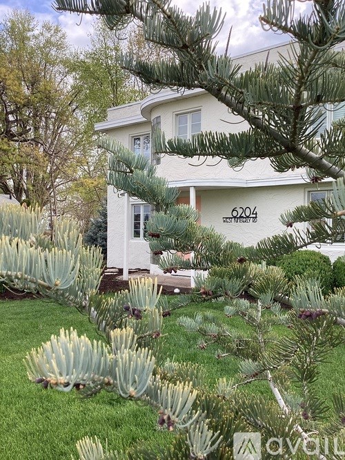 A white house with the number 6204 on it is surrounded by greenery.