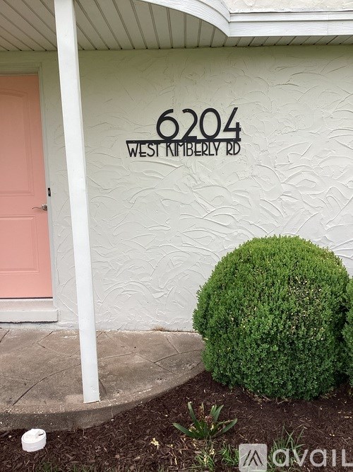 A white house with a pink door and a green bush in front.