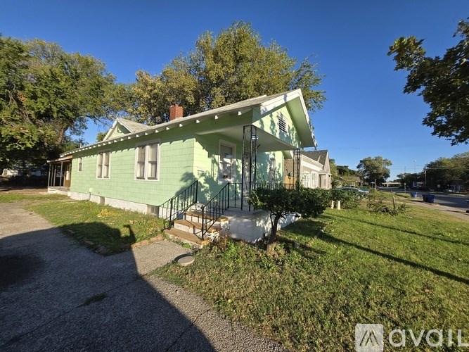 A green house with a porch and a tree in front.