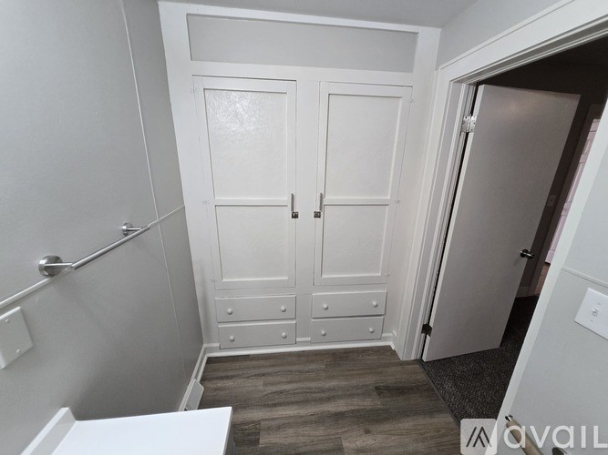 A white bathroom with a toilet, a sink, and a wooden floor.