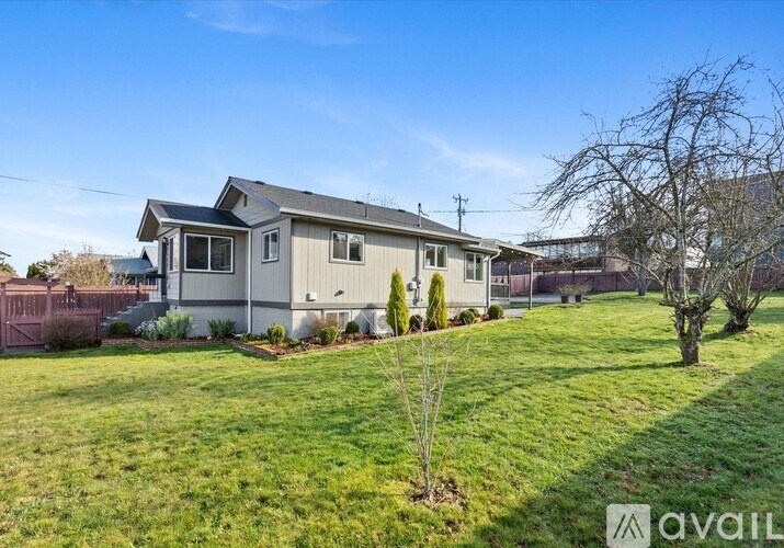 A house with a grey roof and a white fence is surrounded by a green lawn.