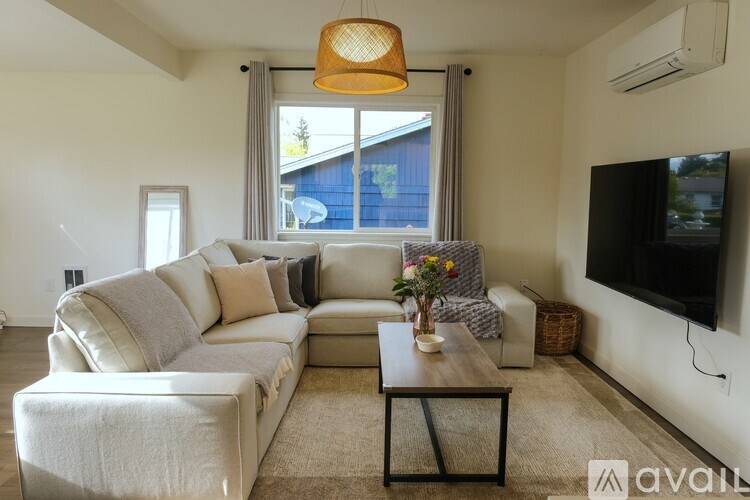 A living room with a large couch, a coffee table, and a flat-screen TV mounted on the wall.