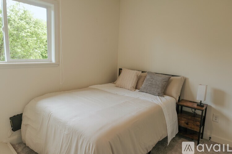A bedroom with a white bed and a window showing greenery outside.